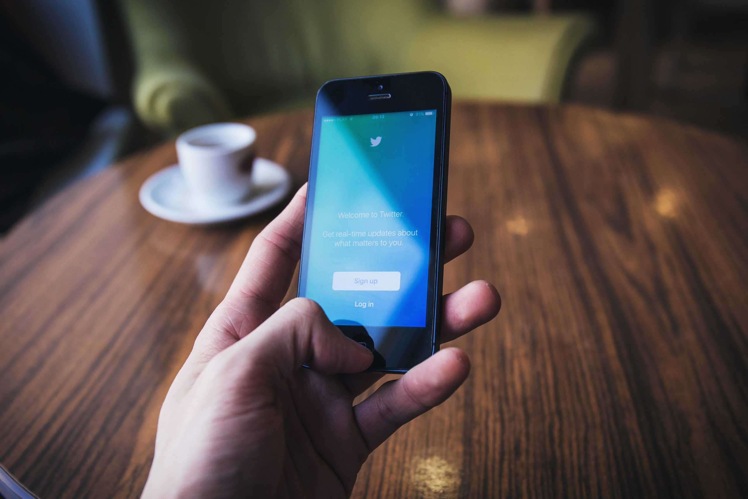 A human hand holding a mobile phone with the Twitter app on the screen