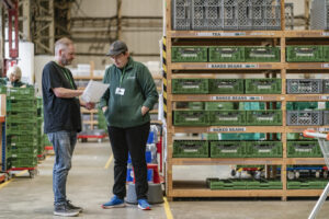 Two men standing in a food bank warehouse looking at a piece of paper.